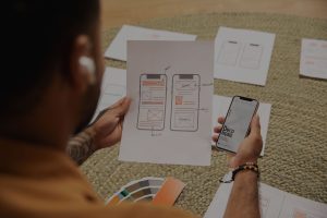 Man holding a mobile phone in one hand and a paper with images of two mobile phones in the other
